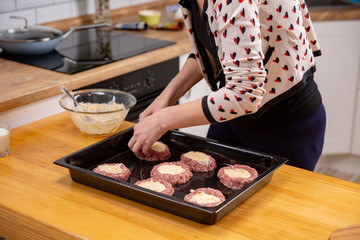 Female hand overlays stuffing theminced meat or meatballs laying on a black baking tray. Process of cooking.