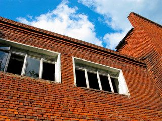 Obraz premium Abandoned brick building, broken and empty windows. Old building in decay. Photo bottom up on the background of blue sky. 