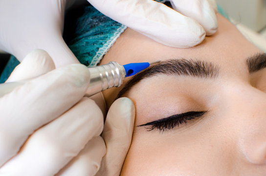 Permanent make-up tattoo, beautician making permanent make up on eyebrows, tattoo procedure on young woman in beauty salon, close up