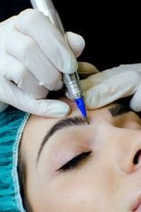 Permanent make-up tattoo, beautician making permanent make up on eyebrows, tattoo procedure on young woman in beauty salon, close up