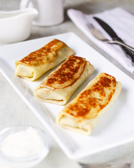 Crepes with chicken and mushrooms close-up on a table and sour cream. Top view, space for text.