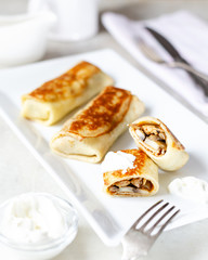 Crepes with chicken and mushrooms close-up on a table and sour cream. Top view, space for text.