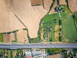 vertical air view of agricultural green fields and lands landscape near a highway and cars on the road