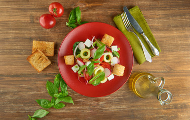 Fresh healthy salad on red plate and basil leaves on wooden table. View from above
