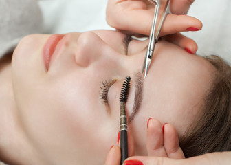 The make-up artist cuts her eyebrows with scissors. A girl with beautiful long eyelashes and...