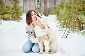Girl in the winter forest walking with a dog. Snow is falling