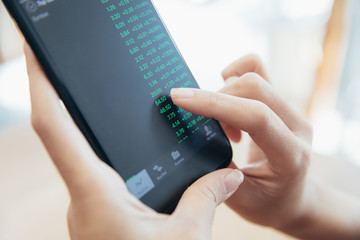 Female hand with smartphone trading stock online in coffee shop , Business concept