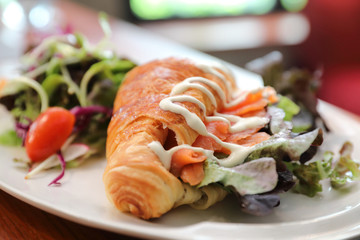 Croissant bread with salmon and salad on wooden background
