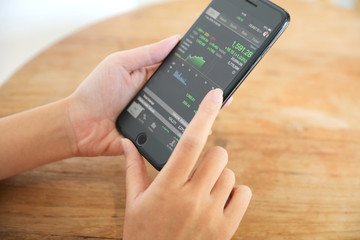 Female hand with smartphone trading stock online in coffee shop , Business concept