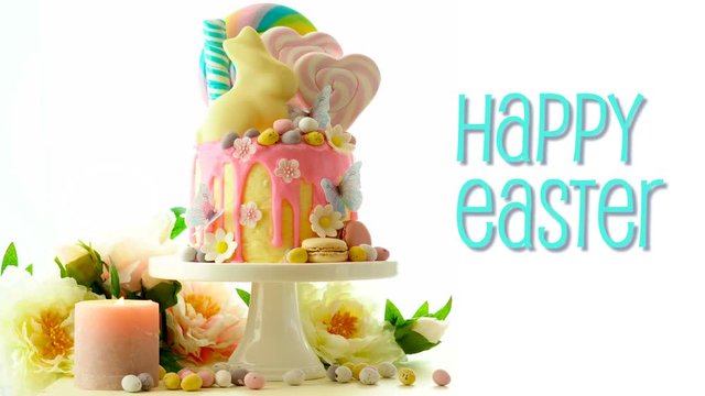 On trend Easter candy land drip cake decorated with lollipops, cand eggs and white chocolate bunny on white background, with animated text greeting.