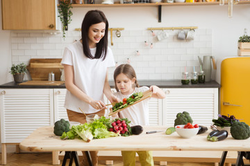 Mother and daughter in preparing healthy vegetables  salad  together  in the kitchen. Help children to parents. 