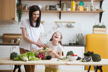 Mother and daughter in preparing healthy vegetables  salad  together  in the kitchen. Help children to parents. 