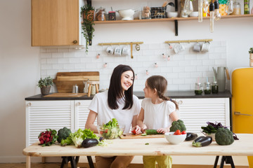 Mother and daughter in preparing healthy vegetables  salad  together  in the kitchen. Help children to parents. 