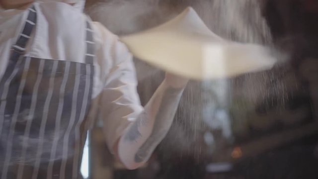 Slow motion of handsome young man spinning and tossing pizza dough up