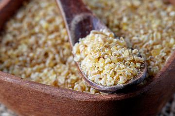 Uncooked raw bulgur wheat grains in wooden bowl