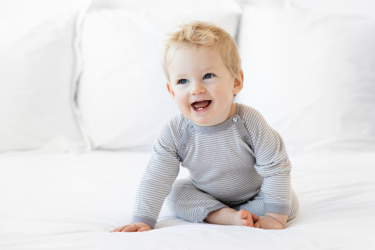 Smiling blonde baby boy sitting on white bed - Powered by Adobe