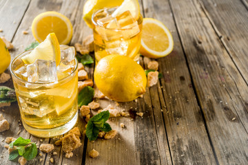 Lemonade or iced summer tea, with fresh lemon slices, sugar and mint leaf, rustic wooden table,...