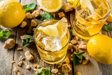 Lemonade or iced summer tea, with fresh lemon slices, sugar and mint leaf, rustic wooden table, copy space