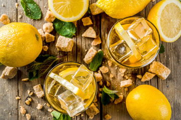Lemonade or iced summer tea, with fresh lemon slices, sugar and mint leaf, rustic wooden table, copy space