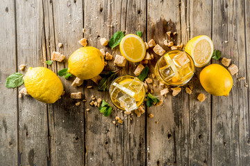 Lemonade or iced summer tea, with fresh lemon slices, sugar and mint leaf, rustic wooden table, copy space