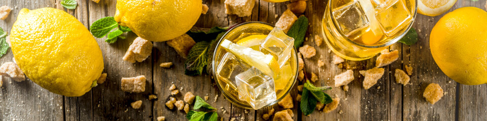 Lemonade or iced summer tea, with fresh lemon slices, sugar and mint leaf, rustic wooden table, copy space banner - obrazy, fototapety, plakaty