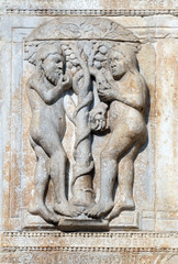 Fototapeta na wymiar Adam and Eve eat the fruit of the forbidden tree, medieval relief on the facade of Basilica of San Zeno in Verona, Italy