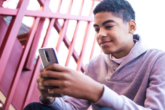 A black man uses a mobile phone. Teen sitting on the stairs playing a game on the smartphone. Afro american boy is writing a message.
