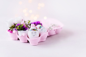 Süße Ostereier mit netten Gesichtern im pinken Eierkarton und Blumendekoration