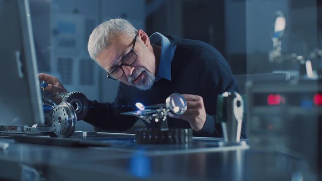 Portrait of Focused Middle Aged Engineer in Glasses Working with High Precision Laser Equipment, Using Lenses and Testing Optics for Accuracy Required Electronics