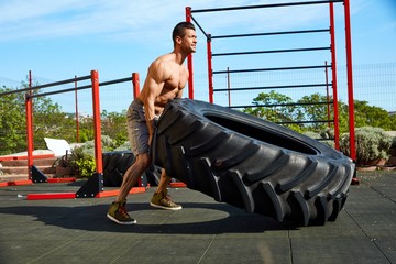Muscular man rolling a tyre at outdoor gym
