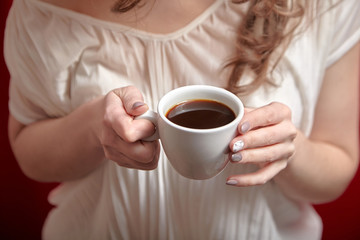 White cup of black coffee in female hands