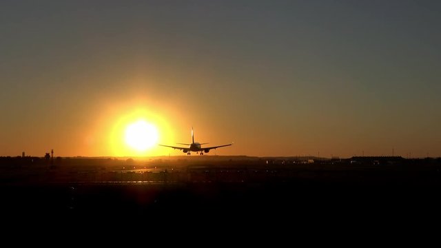 4K. Commercial airplane is landing on the airport runway during sunset. The sky is orange. Silhouette of an airplane that is landing.