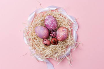 Easter eggs in nest with white ribbon on pink background. Easter texture