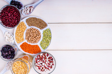 Different beans in bowls on a white wooden table, top view