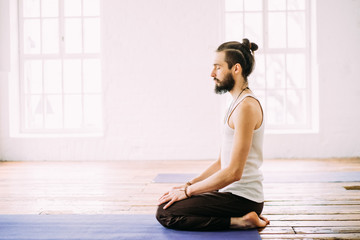 Man sit with closed eyes in studio with wooden floor and big windows. Mediation. Concept of healthy...
