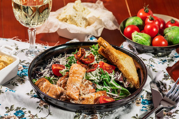 Caesar Salad with Grilled Salmon on Elegant Restaurant Plate. Served with white wine. Salat with Red Fish Fillet, Crackers, Cherry Tomatoes, Lettuce Leaves, Caesar Sauce and Parmesan Cheese