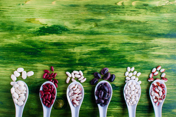 various dried legumes in wooden spoons on green background