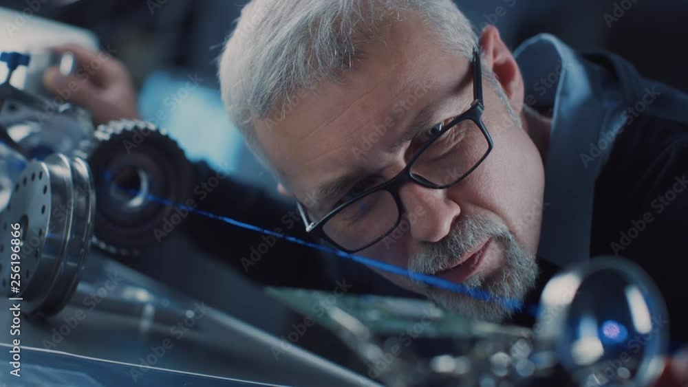 Poster Close-up Portrait of Focused Middle Aged Engineer in Glasses Working with High Precision Laser Equipment, Using Lenses and Optics for Accuracy Electronics. 