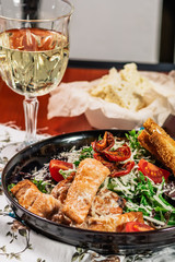 Caesar salad with salmon. Served with white wine. Salad with red fish fillet, cesar sauce, croutons, lettuce, cherry tomato, close up.