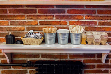 Close-up view of various disposable wooden sticks, wooden spoon, tooth sticks, cup covers, Take away boxes, napkins and sugar bags on wooden counter in cafe for self-service and take away drinks