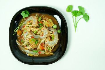 Spicy Papaya salad with raw shrimp in black plate. Isolated white background 