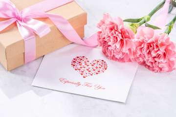 May mothers day handmade giftbox idea concept, beautiful blooming carnations with baby pink ribbon bow gift isolated on modern marble desk, close up, copy space, mock up