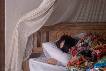 Woman sleeping in sleep mask under a patchwork blanket.