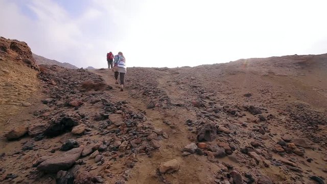 A group of tourists walking throught the colored deserted rocky hill. Hormuz Island. Iran