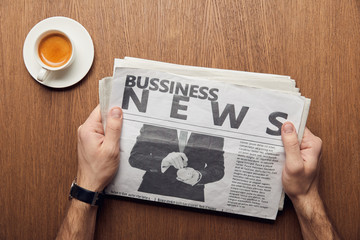cropped view of man holding business newspaper near cup of coffee