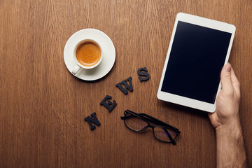 Obraz na płótnie Canvas cropped view of man holding digital tablet with blank screen near news lettering, cup of coffee and glasses