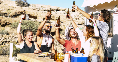 Fun success and friendship concept with group of young men and women people all together toasting with beers and food sitting on a rural wood table with nature in background