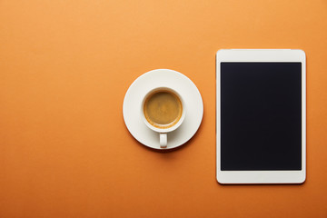 Fototapeta na wymiar top view of digital tablet with blank screen near cup of coffee on orange