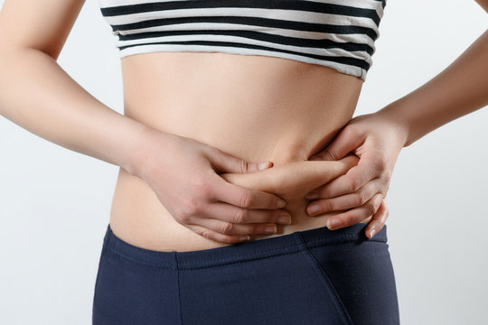 a young woman feels with two hands folds on her stomach. On light white background. Concept of weight loss, proper nutrition, excess weight, women's health