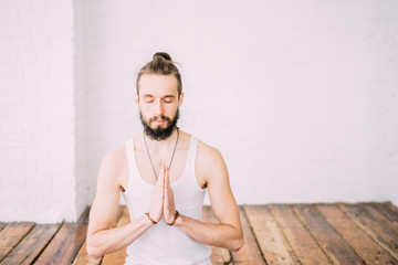 Man sit in lotus in yoga studio with wooden floor and white wall. Mediation. Concept of healthy...